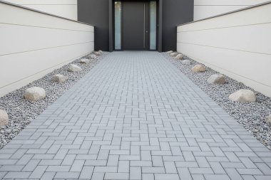 Bu resimde modern bir ev girişi, şık bir yürüyüş yolu ve çekici peyzaj unsurları yer alıyor.