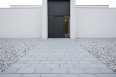 Çağdaş bir bina girişinde karanlık bir kapı, taş bir patika ve temiz, modern bir estetik oluşturan çakıllı bir sınır bulunur.