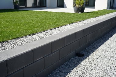 Bu resim, bir istinat duvarı, çakıl ve yemyeşil çimlerin yer aldığı çağdaş bir manzara tasarımı sergiliyor.