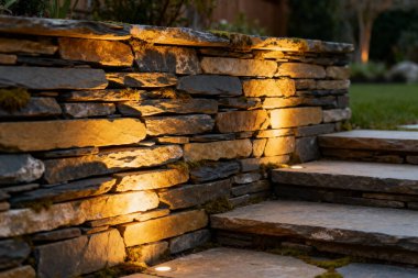 Ilık aydınlatma, doğal bir taş duvar ve basamakları aydınlatır. Açık havada hoş geldin ortamı yaratır.