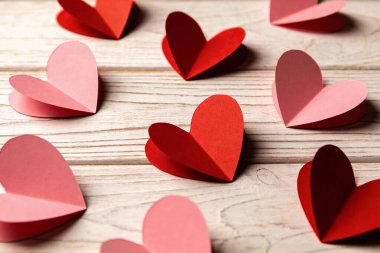 Yıpranmış ahşap bir yüzey üzerinde ustalıkla dizilmiş canlı kırmızı ve yumuşak pembe renkte katlanmış kağıt kalpler koleksiyonu.