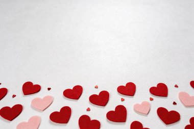 Kırmızı ve açık pembe küçük keçeli kalplerden oluşan bir derleme beyaz desenli bir yüzeye yayılarak şenlikli ve romantik bir atmosfer yaratıyor.