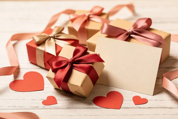 Saten kurdeleler ve kırmızı kağıt kalplerle süslenmiş bir hediye kutusu koleksiyonu. Kırsal ahşap bir yüzeye karşı dizilmiş. Kutlamalar için mükemmel.