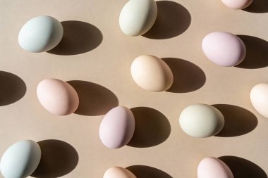 Renkli pastel yumurtalardan oluşan bir koleksiyon. Hoş bir şekilde düzenlenmiş. Tarafsız bej bir yüzeye farklı gölgeler bırakıyor.