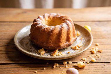 Taze pişmiş bir kek, üzerine pudra şekeri serpiştirilmiş ve kırıntılarla çevrili, leziz bir ziyafeti ima eden dokulu bir tabakta oturur.