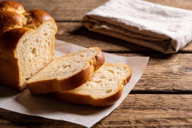 Dilimlenmeye ve eğlenmeye hazır altın-kahverengi bir somun ekmek eskimiş ahşap bir yüzey üzerindeki parşömen kağıdının üzerinde duruyor.