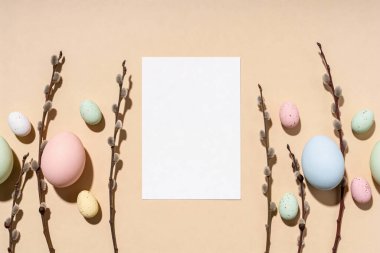 A festive arrangement of pastel Easter eggs and delicate pussy willow branches frames a blank white card, perfect for spring greetings
