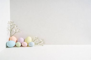 Pastel renkli Paskalya yumurtaları ve bebek nefesinin dalları minimalist beyaz bir boşluğun köşesinde ustalıkla düzenlenmiştir.
