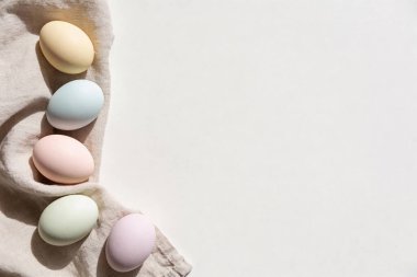 Zarif renklerde Paskalya yumurtaları, yumuşak güneş ışığıyla yıkanmış ve yumuşak gölgeler oluşturan tarafsız bir kumaş yüzeyine dayanır.