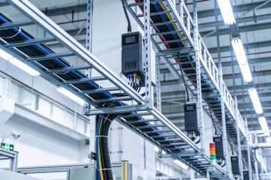 Metal tepsilerde düzgün bir şekilde düzenlenmiş karmaşık kablo ve kanallar ağı, bir üretim tesisinde verimli altyapıyı vurguluyor