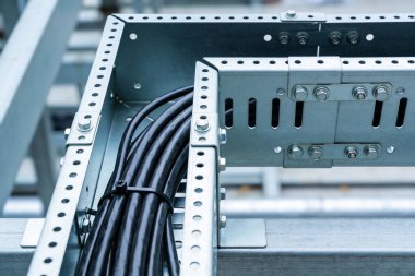 Siyah elektrik kablolarının yakın plan görüntüsü birbirine bağlanmış ve delinmiş metal kablo yönetim tepsisinin içine kablo bağıyla bağlanmış.