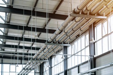 Modern endüstriyel bir binanın tavanından geniş pencerelerden gelen doğal ışıkla aydınlatılan esnek metal borular askıya alınır.