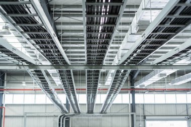 Metal kablolar ve hava kanallarından oluşan karmaşık bir ağ büyük bir endüstriyel binanın tavanında düzgünce düzenlenmiştir.