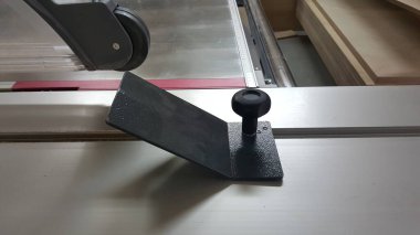 Bir ahşap atölyesinde kullanıma hazır metal bir masa testeresi çitinin üzerine siyah bir itme bloğu yerleştirildi.