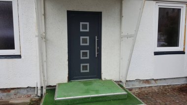 Çağdaş bir giriş. Koyu gri bir kapı. Buzlu camlar ve parlak metal bir sapı var.