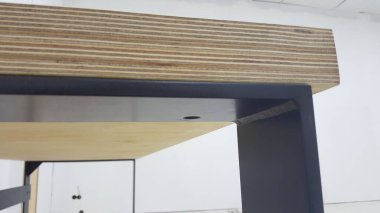 Çağdaş bir masanın katmanlı kontrplak kenarı ve koyu metal çerçevesinin yakın görüntüsü, inşaatını gösteriyor.