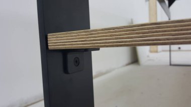 Ayrıntılı bir görünüm görünür vida ve parantez ile mat siyah metal desteğine sabitlenmiş bir kontrplak rafının katmanlı dokusunu gösterir