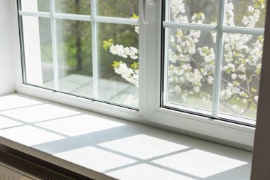 Pencerenin dışındaki ağaçta beyaz kiraz çiçeklerini gösteren parlak, güneşli bir pencere pervazı.