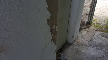 Dış duvardaki hasarlı alçıyı yakından görmek, altında sert bir dokuyu, bir kapı aralığı ve tuğla cephesi olduğunu ortaya çıkarıyor.