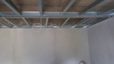 Askıya alınmış bir tavan için çıplak metal çerçeve görünür, alçıpan kurulumu ve elektrik bileşenleri bekliyor