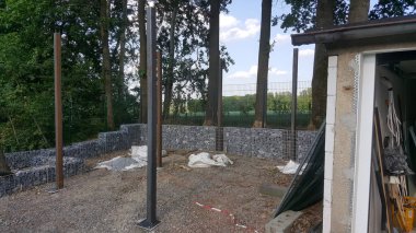 Gabion istinat duvarları ve dikey metal direklerin yer aldığı açık hava inşaat alanı, devam eden gelişimi veya peyzaj çalışmalarını gösteriyor