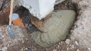 İnşaat alanı, metal ağ ve borunun etrafındaki bir çukura ıslak çimento döküldüğünü gösteriyor.