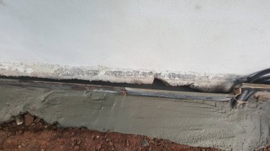 Görünür elektrik kabloları ve kabloları olan hasarlı duvar tabanına taze beton uygulandığını gösteren bir inşaat alanının yakın görüntüsü.