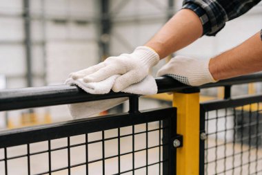 Koruyucu eldivenler giyen bir kişi, endüstriyel bir ortamda hijyen ve bakımı vurgulayan beyaz bir bezle siyah bir metali titizlikle temizler.