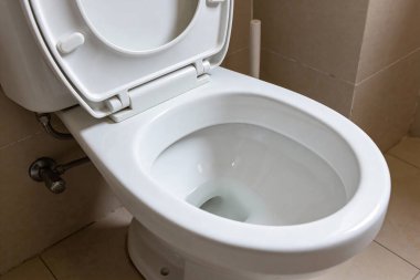 Kapağı ve kapağı kaldırılmış, temiz iç ve su tesisatı bağlantılarını gösteren el değmemiş beyaz bir seramik klozetin yakın görüntüsü.