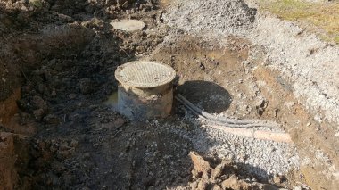 İnşaat alanı açık bir siper gösteriyor. Somut bir kamu hizmetleri erişim yapısı ve çevresindeki borular yeraltı altyapı çalışmalarını gösteriyor.