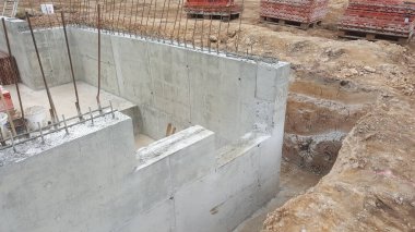 Güçlendirilmiş beton duvarlar inşaat sahasında kısmen inşa edilir, açıkta kalan demirler ve yakınlarda kazılmış toprak