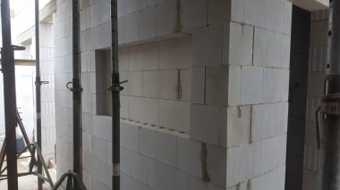 İnşaat halindeki bir binanın iç manzarası, beyaz beton bloklar ve destek ve istikrar için kullanılan metal iskeleler.