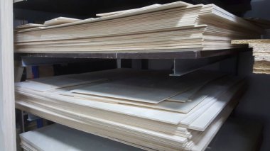 Büyük miktarda açık renkli ahşap paneller metal raflarda depolanmış, inşaat veya el yapımı projelerde kullanılmaya hazır.