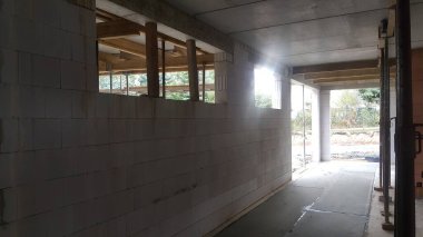İnşaat halindeki bir binanın iç manzarası, beton zemini, beton blok duvarları ve ahşap destek kirişlerini gösteriyor.