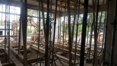 İnşaat alanı, beton yapı çalışmalarını destekleyen sayısız metal iskele direği ve ahşap kirişlerle gösteriliyor.