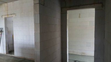 Beyaz beton bloklardan ve açık kapılardan yapılmış duvarların yer aldığı tamamlanmamış iç alan, bir inşaat veya yenileme aşamasını işaret ediyor