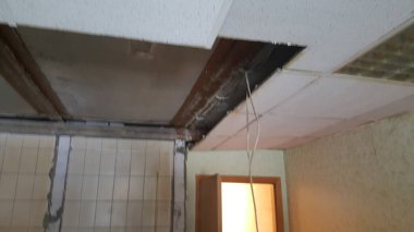 Asılı tavanın bir kısmı eksik. Tahta kirişler ve elektrik kablolarını gösteriyor. Odada devam eden inşaat ya da ihmal olduğunu gösteriyor.