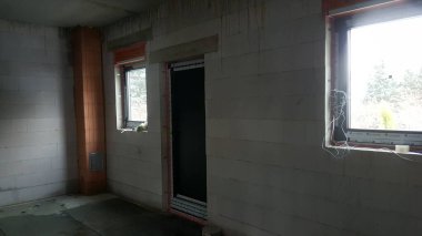 İnşaat halindeki bir binanın tamamlanmamış iç kısmı beton blok duvarlar, pencere çerçeveleri ve tamamlanmayı bekleyen bir kapı.