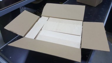 Açık bir karton kutu, içinde düzgünce düzenlenmiş, kullanılmaya ya da taşınmaya hazır, bitmemiş birkaç tahta parçası gösterir.