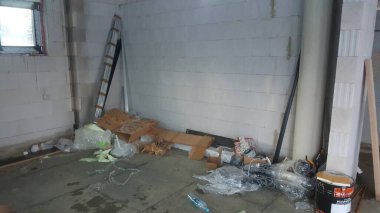 Karton kutular, plastik ambalajlar ve inşaat halindeki bir odanın dağınık bir köşesinde yığılmış yapı malzemeleri.