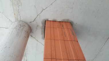 Görünür çatlaklar, geniş silindirik bir boru ve yapıya entegre edilmiş turuncu bir terakotta havalandırma şaftı olan tamamlanmamış beton tavanın yakın görüntüsü.