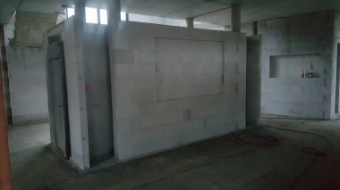 Tamamlanmamış iç mekan, tuğla duvarlar, kapılar ve açık tavan kirişleri ile inşaat halindeki bir binayı gösteriyor.