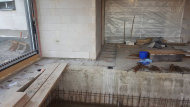 Bitmemiş bir binanın içinde beton iş, çelik takviye çubukları ve inşaat malzemeleri görülüyor. Bu da devam eden gelişmeyi ve yapısal ilerlemeyi gösteriyor.