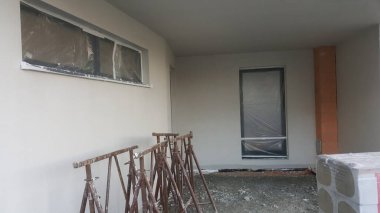 Görüntü, tamamlanmamış dış duvarları, örtülü pencereleri ve yapı iskelesi olan inşaat halindeki bir binayı gösteriyor.