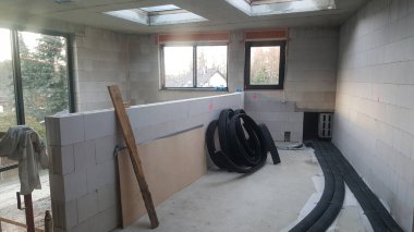 Beton blok duvarları, çatı pencereleri, pencereleri ve borular ve ahşap tahtalar gibi çeşitli inşaat malzemeleri olan bir oda.