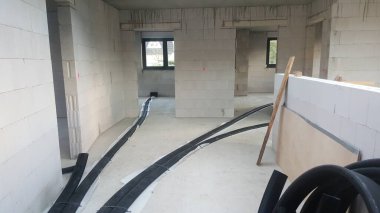 Tamamlanmamış bina içi beton duvarlar, beton zemin ve kurulum için siyah yalıtılmış borular.