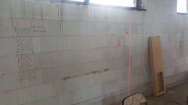 Bir inşaat sahasında tebeşir çizgileri, lazer seviyesi ve el yazısı notları olan ve gelecekte yapılacak iş planlarını gösteren beton blok bir duvar var.