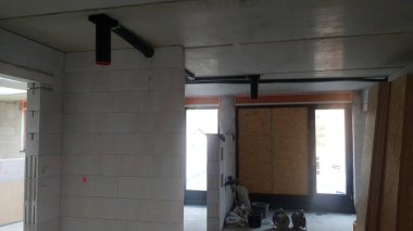 Yapım aşamasındaki bir binanın tamamlanmamış iç yapısı, açıkta kalan boru sistemleri ve beton blok duvarları, devam eden kalkınma ve yenileme süreçlerini gösteriyor