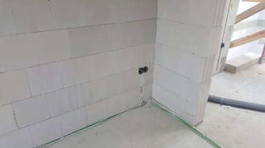 İnşaat halindeki bir binanın tamamlanmamış iç kısımları, havalandırılmış beton bloklar, zemindeki elektrik kabloları ve kabloları sergileniyor.