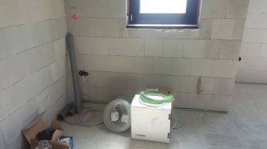 İnşaat halindeki bir binanın içinde tuğla duvarlar, tesisat boruları, kablo makaraları ve montajı bekleyen elektrik parçaları yer alıyor.